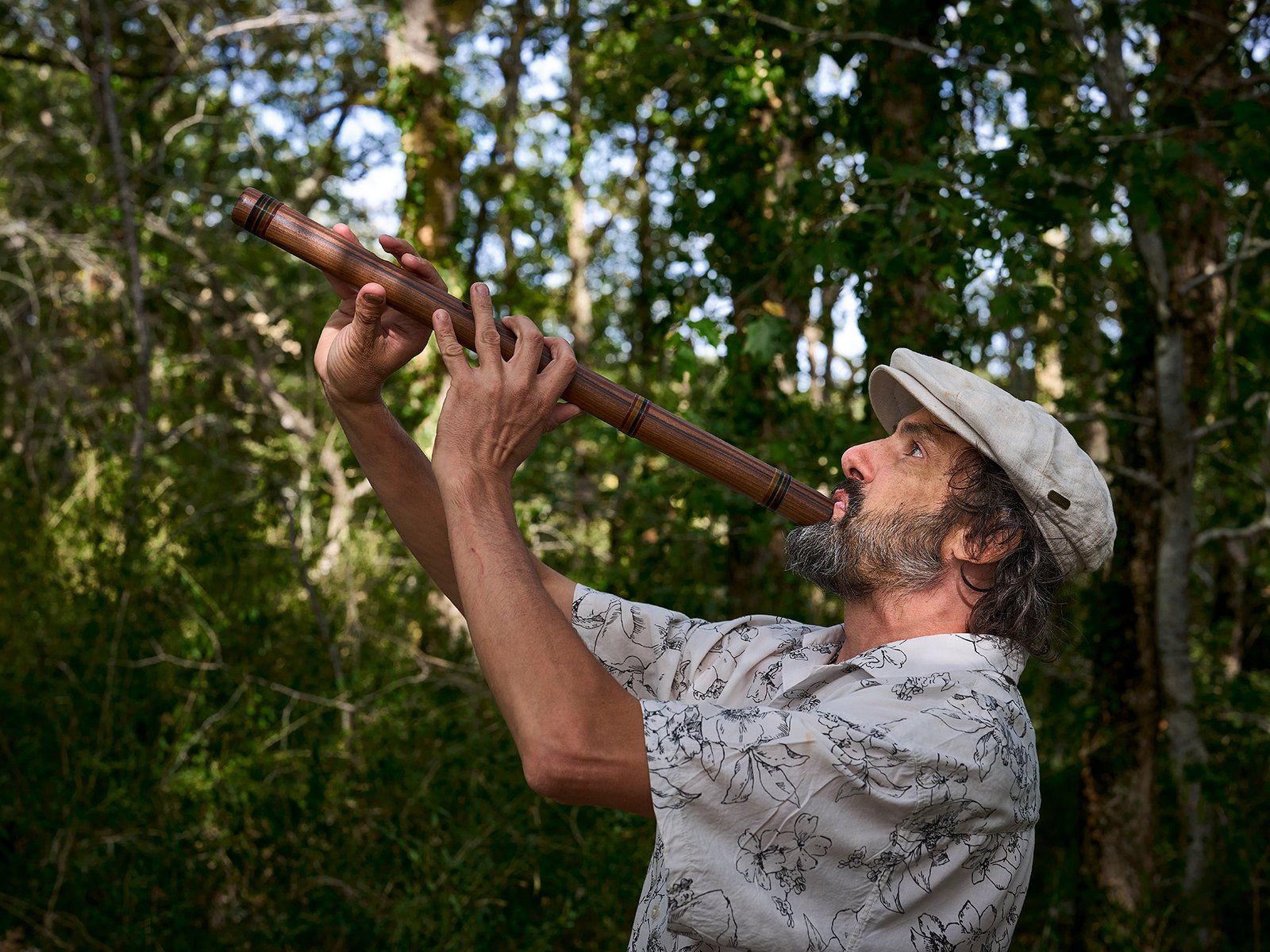 Eliah Jasper playing a long wooden instrument among trees