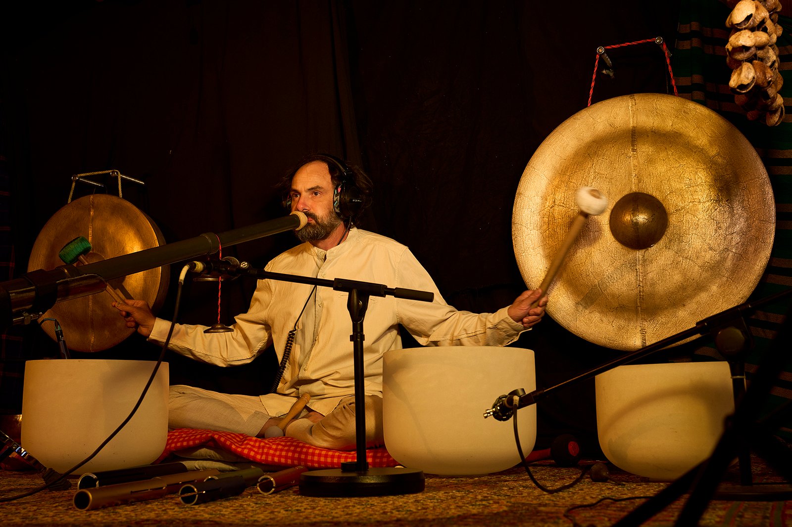 Eliah Jasper performing live with headphones beside a large golden gong and crystal bowls