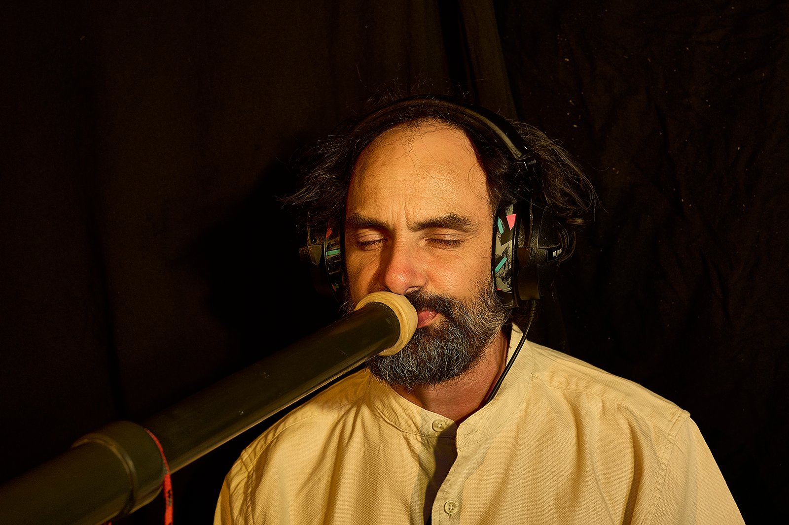 Portrait of Eliah Jasper with headphones and microphone in a dark studio